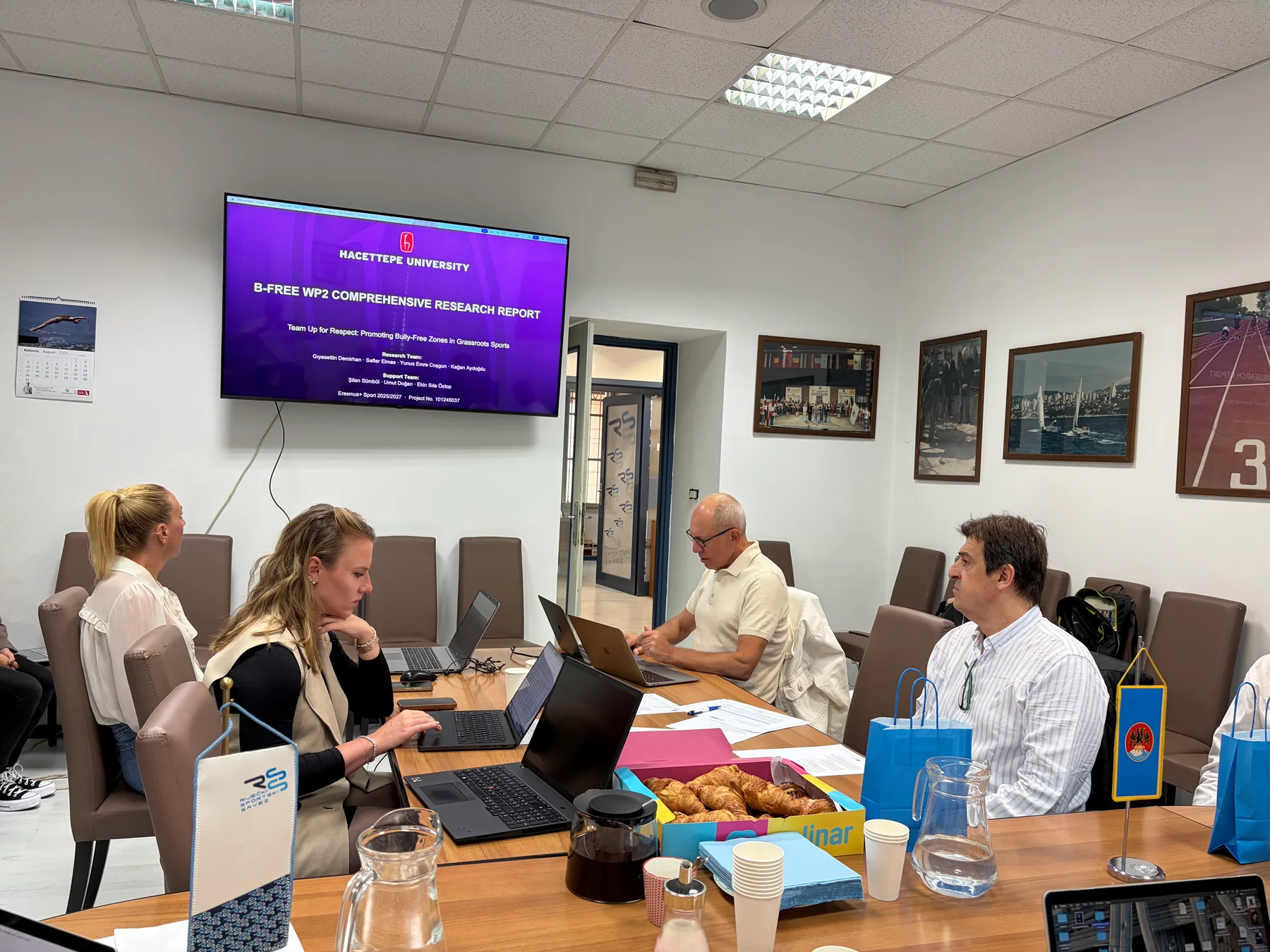 B-FREE partners seated around a meeting table in Rijeka, with Hacettepe University's WP2 Comprehensive Research Report displayed on screen.